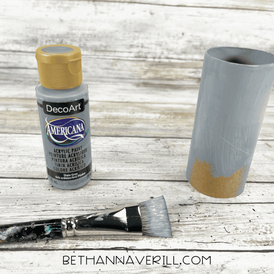 Toilet paper roll painted gray with paintbrush and paint bottle beside it.