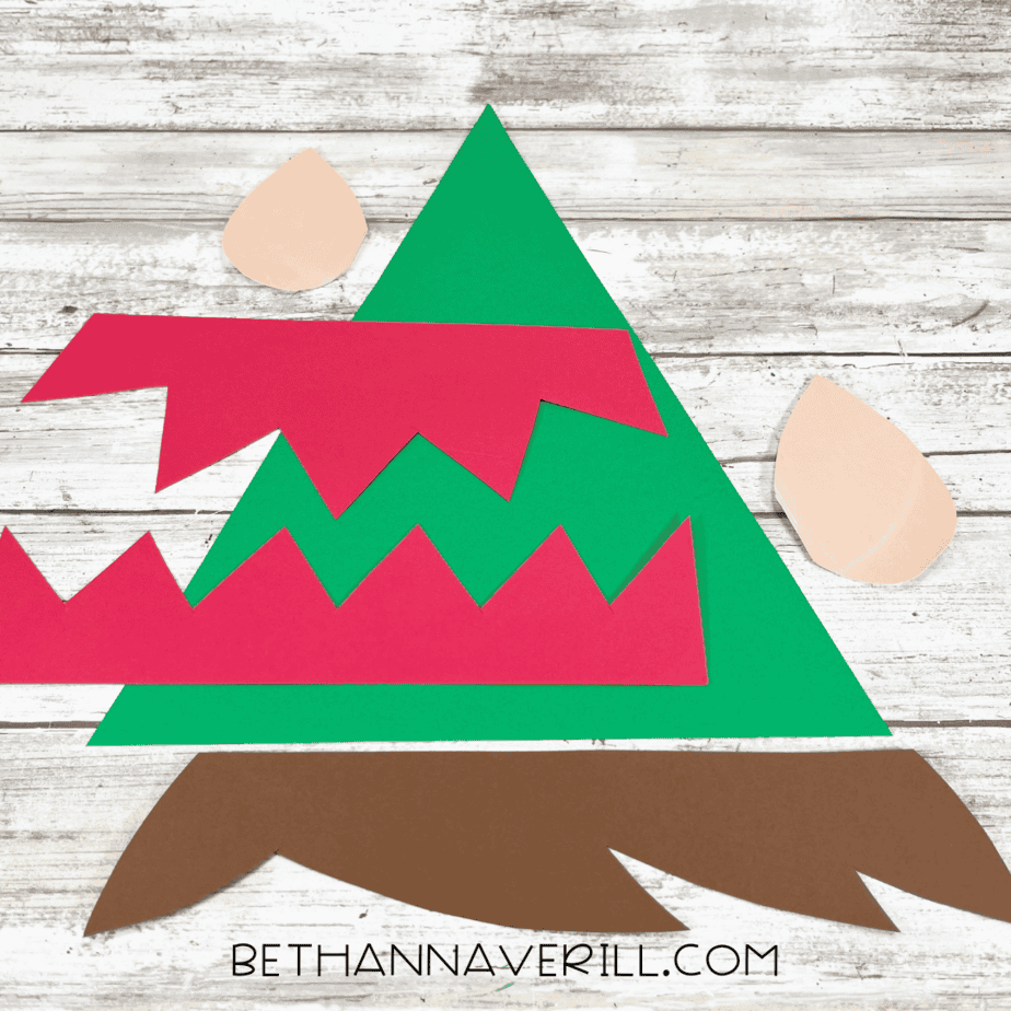 Cut paper pieces for elf hat, trim, and ears laid out on the table.