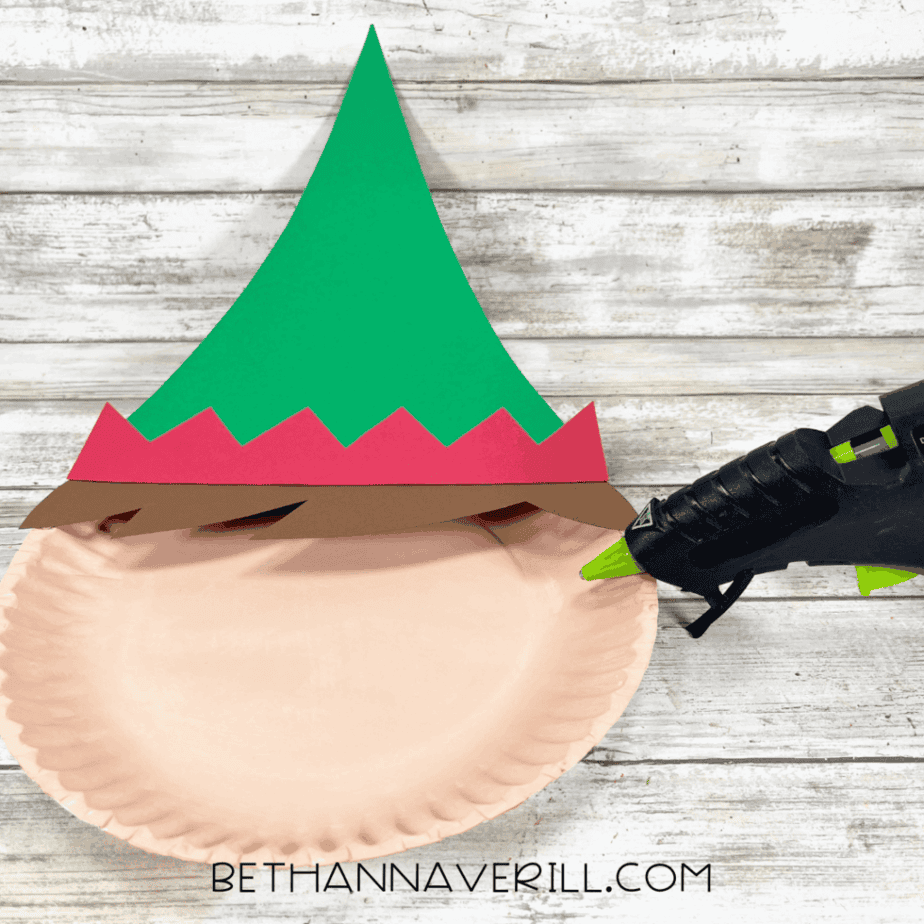 Paper plate with green hat, red trim, and brown hair glued on top.