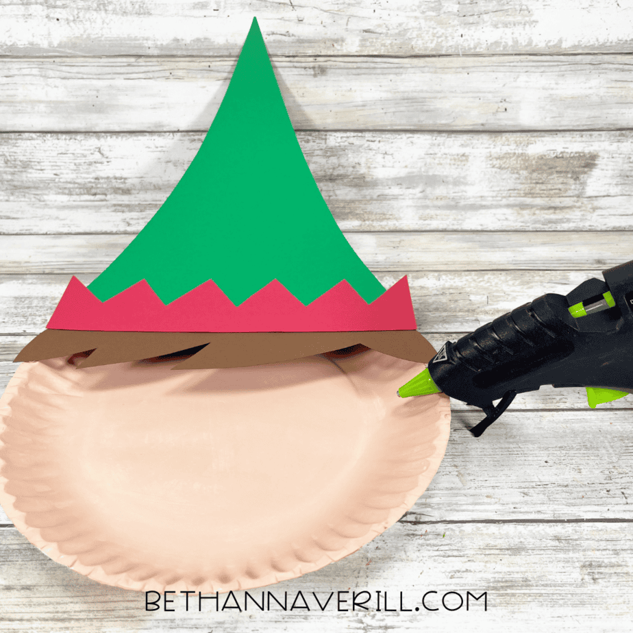 Paper plate with green hat, red trim, and brown hair glued on top.