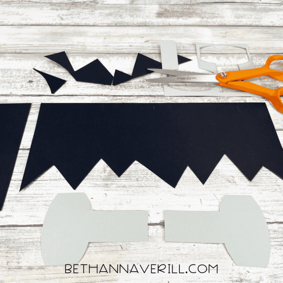 Cut out black jagged hairpiece and gray paper bolts with orange scissors.