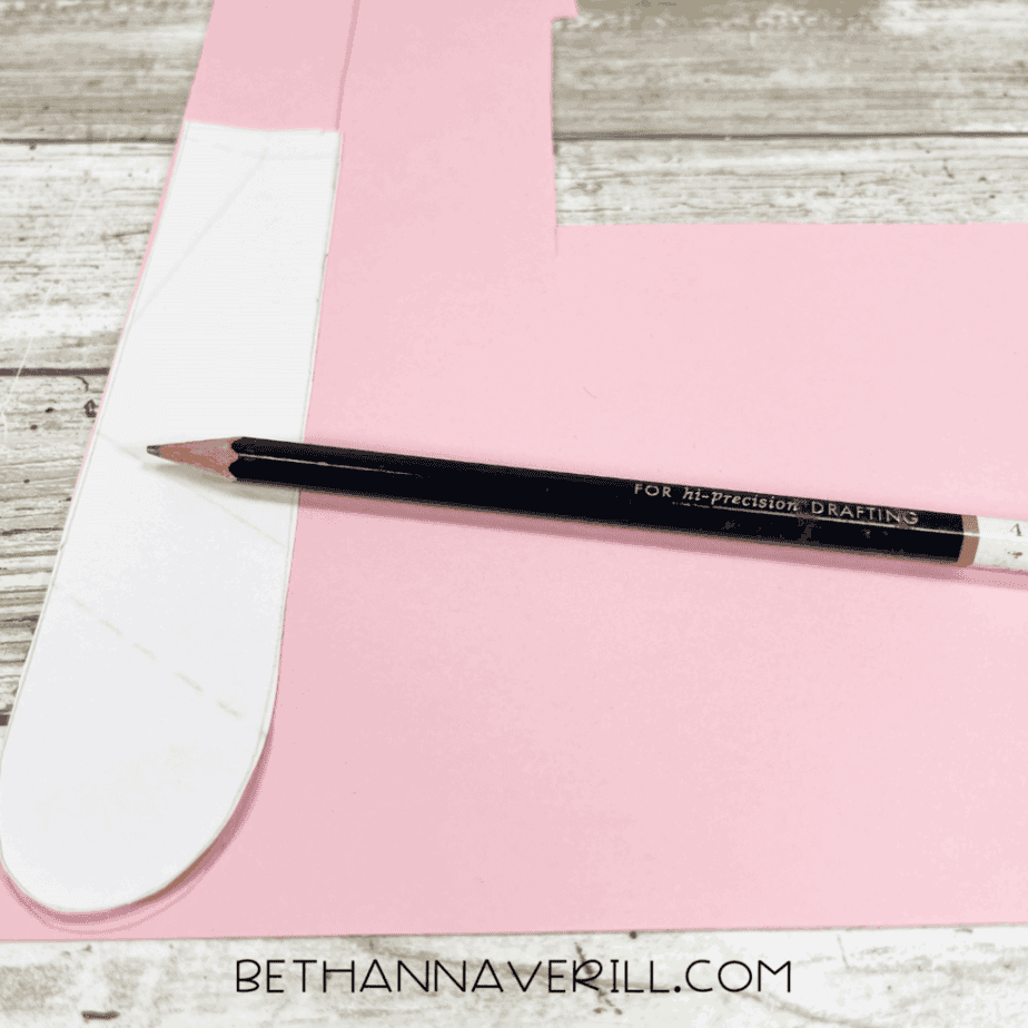 A pencil tracing a tongue shape on pink construction paper.