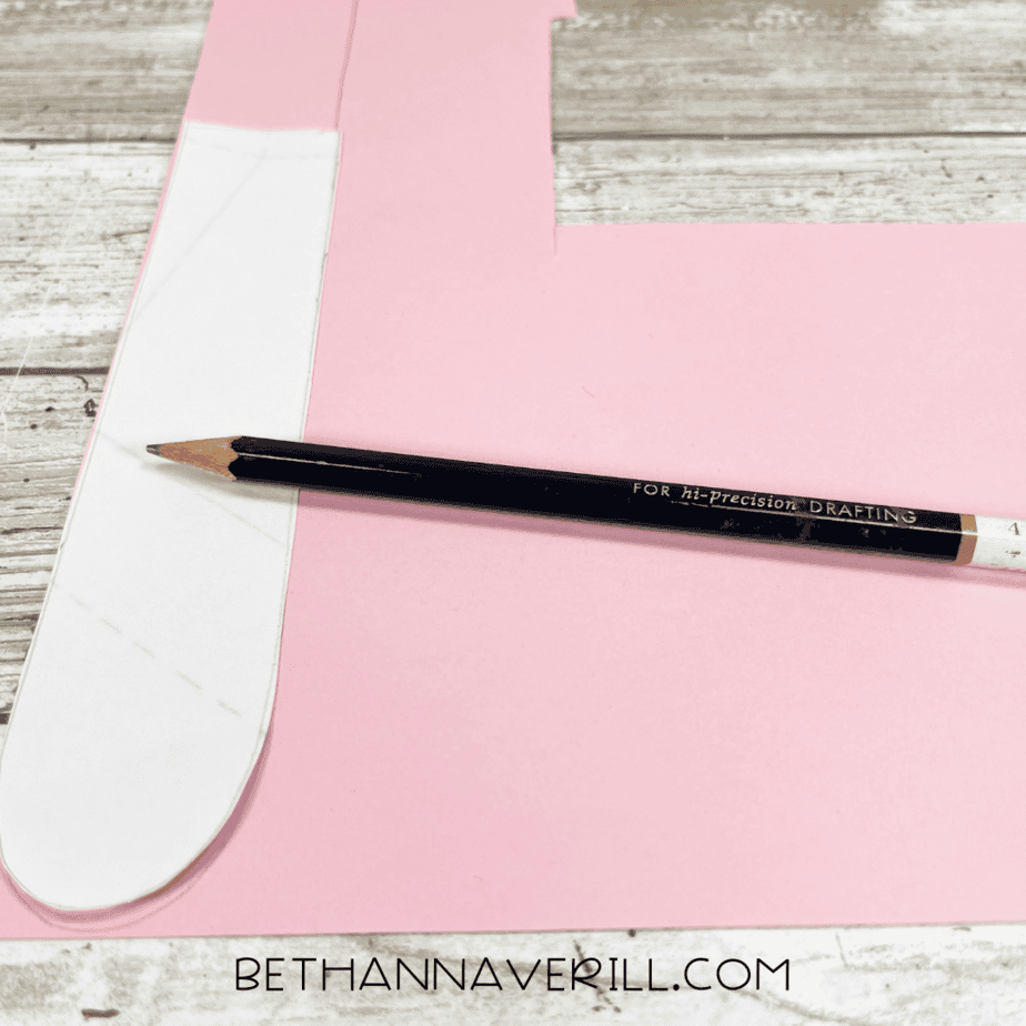 A pencil tracing a tongue shape on pink construction paper.
