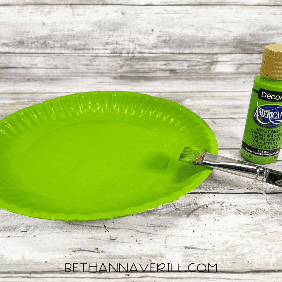 A paper plate painted bright green with a paintbrush resting on the edge.