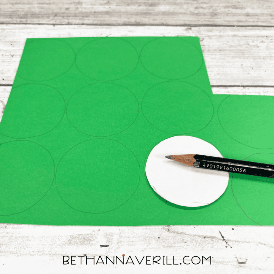A pencil tracing circles onto green construction paper using a small round template.