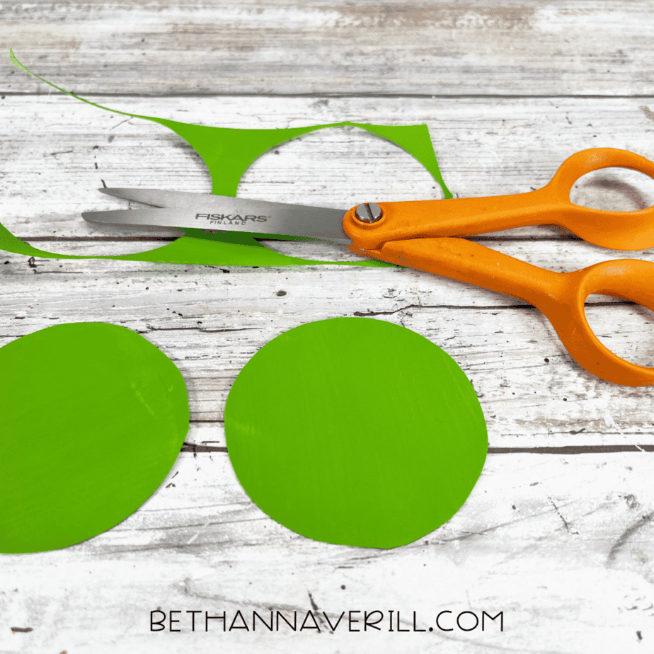 Orange scissors cutting out large green circles from the construction paper.