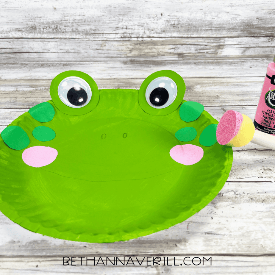 A sponge dabber painting pink circles onto the frog’s face for rosy cheeks.