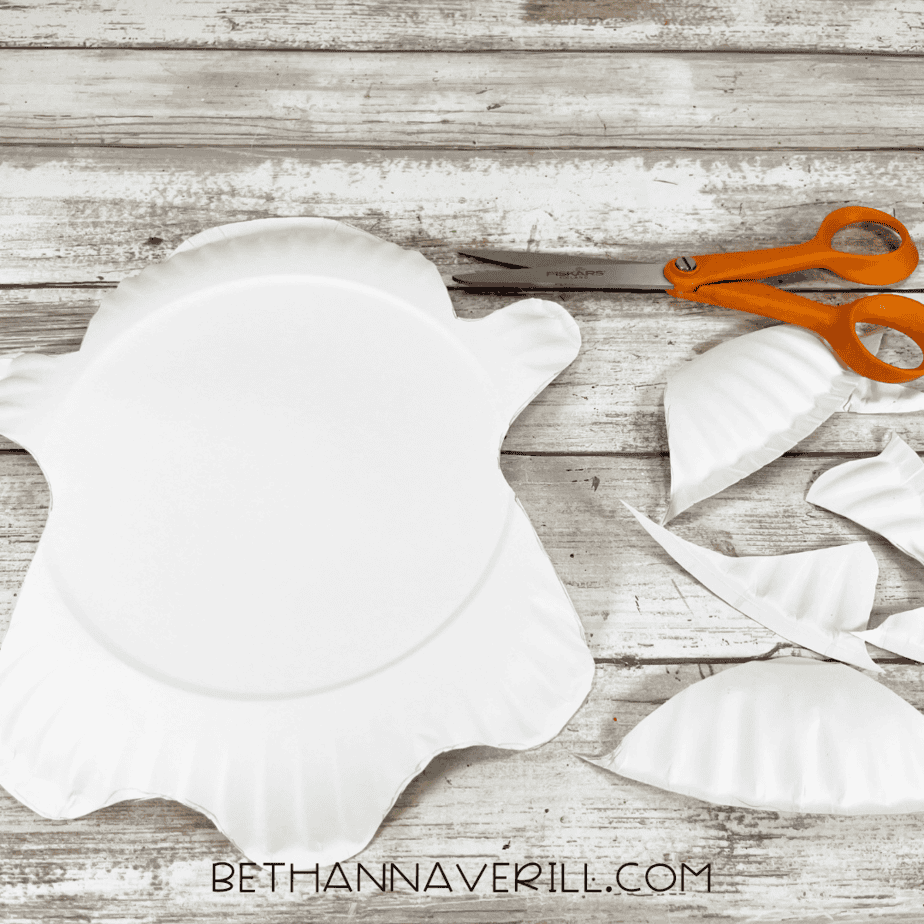 A large paper plate cut into the shape of a ghost with rounded arms and wavy edges.