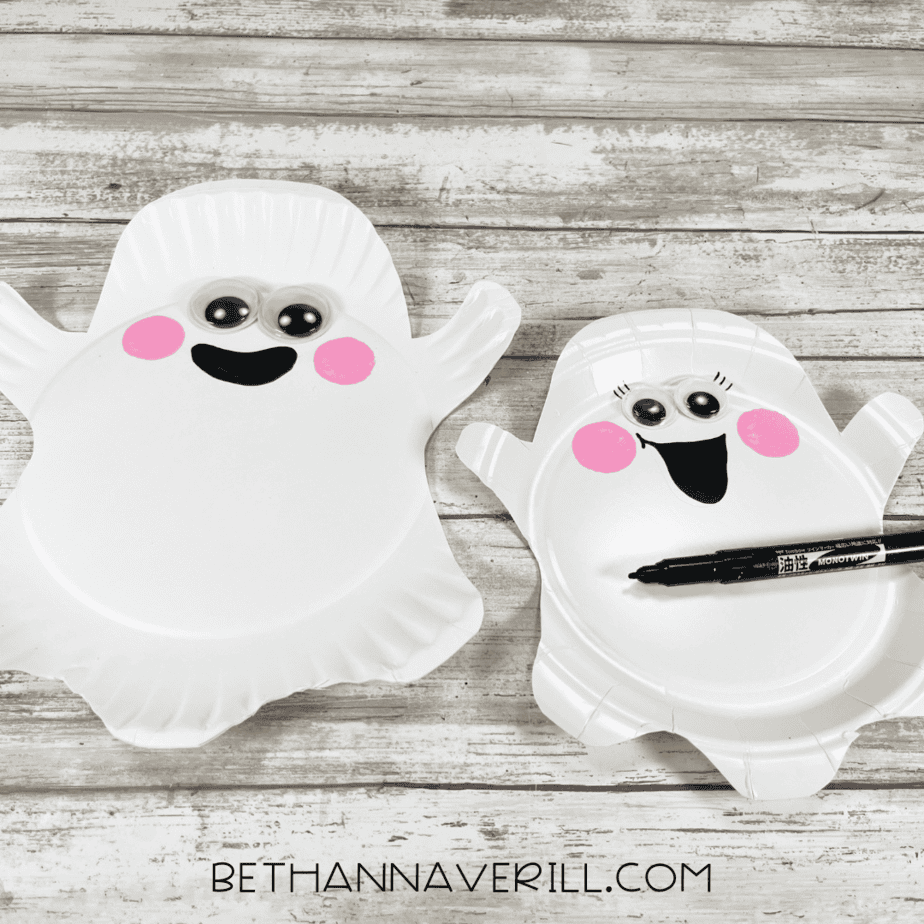 Two paper plate ghosts with black marker smiles drawn, one with added eyelashes.
