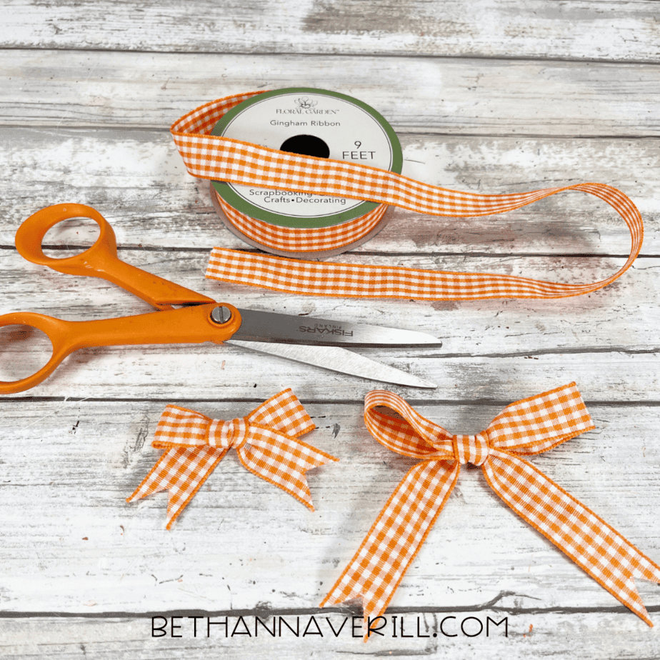 Orange gingham ribbon being cut and tied into small bows with scissors.