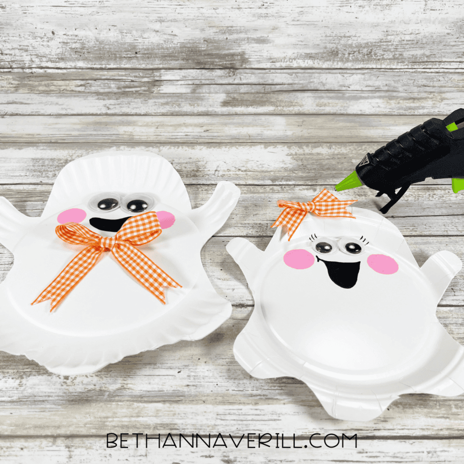 Paper plate ghosts with orange bows glued on, one under the chin and one on the head.