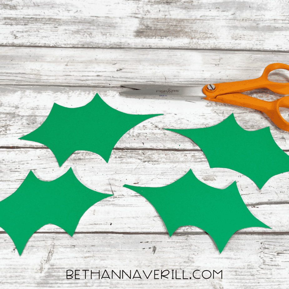 Green holly leaves cut out and placed on the table.