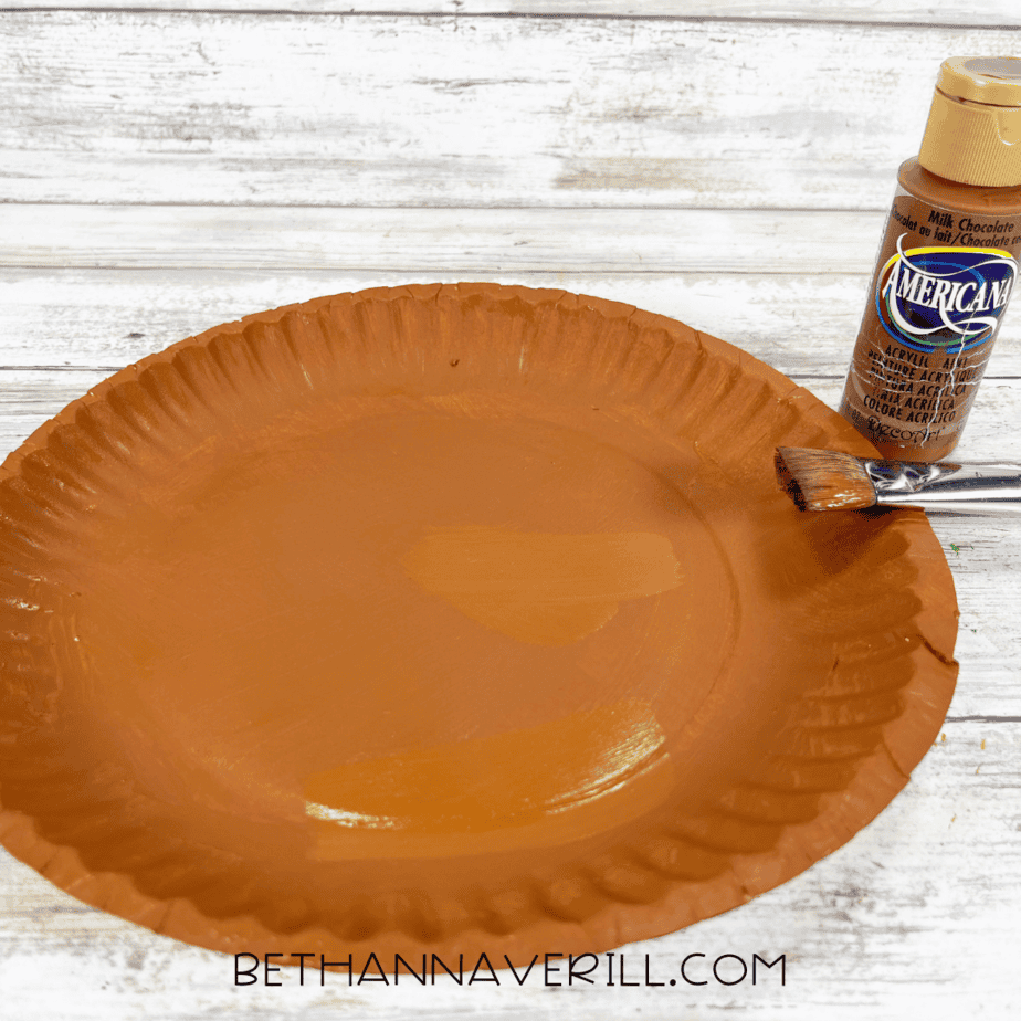 Paper plate painted brown with a paintbrush beside it.