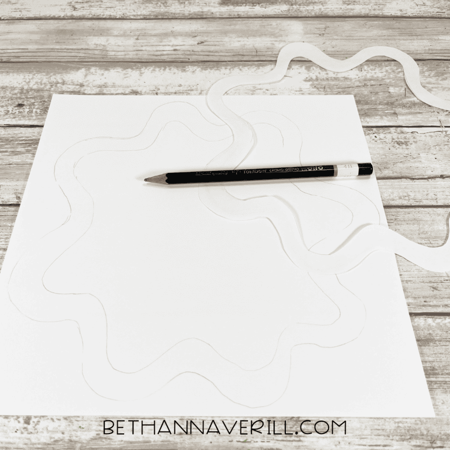 Pencil tracing a wavy icing design on white paper.