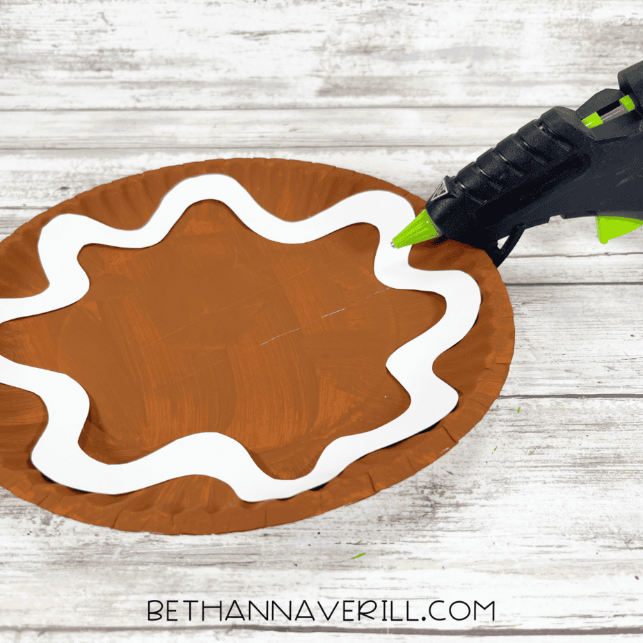 White icing trim being glued onto a brown painted paper plate.