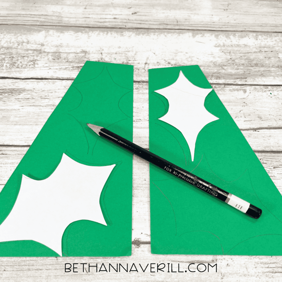Pencil tracing holly leaf shapes on green construction paper.