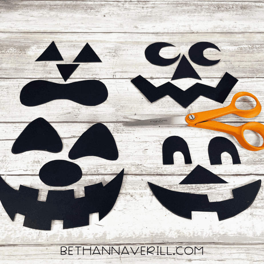 Black paper jack-o’-lantern face shapes cut out and arranged on a table.