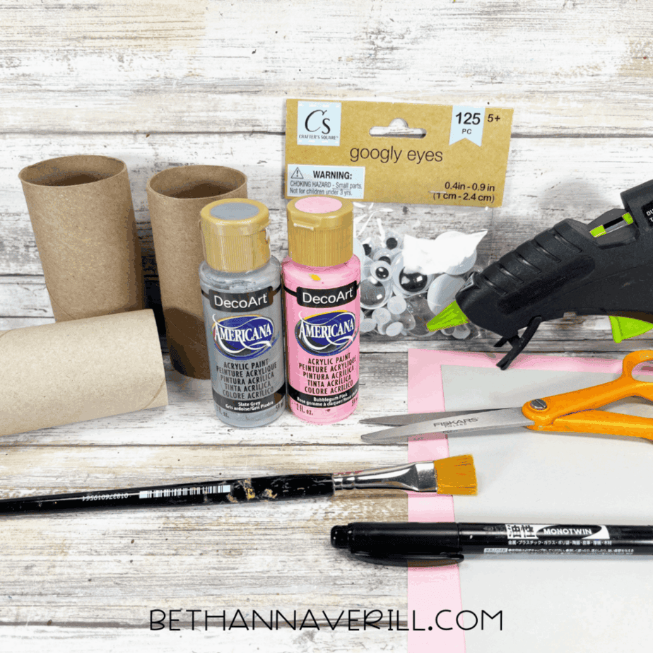 Materials for koala paper roll craft, including toilet paper rolls, paints, googly eyes, scissors, glue gun, and paper.