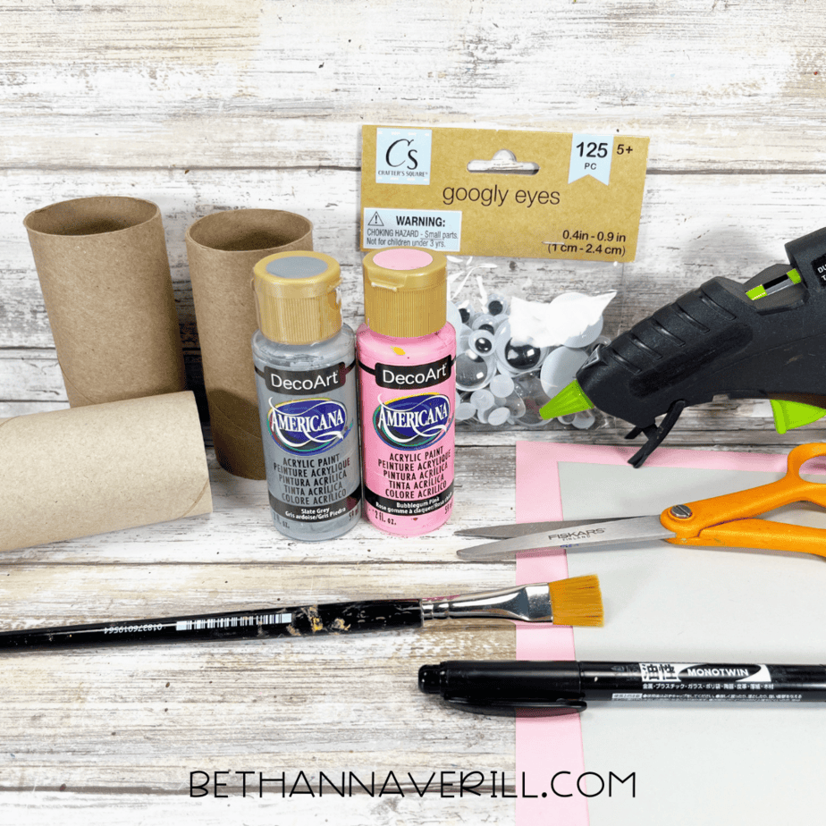 Materials for koala paper roll craft, including toilet paper rolls, paints, googly eyes, scissors, glue gun, and paper.
