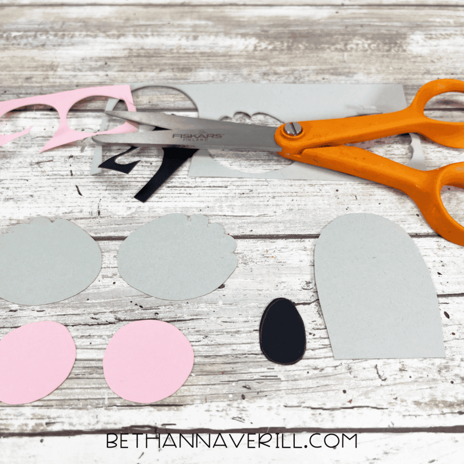 Cut out koala shapes in gray, pink, and black paper with orange scissors on a table.