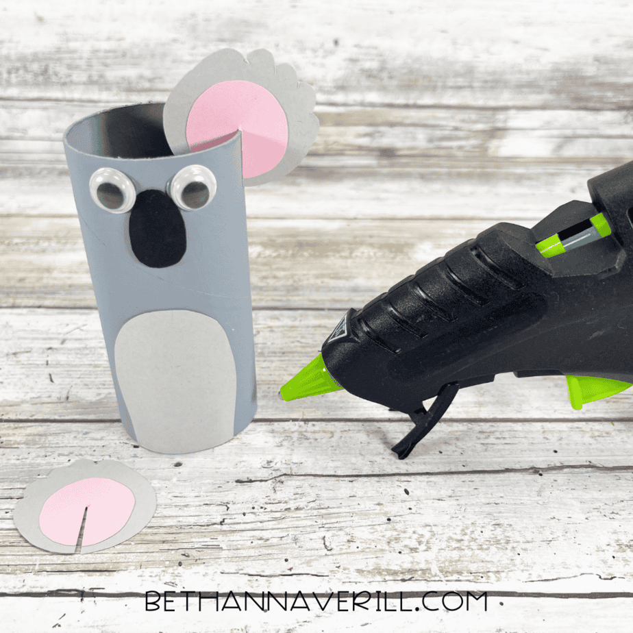 One ear with pink circle glued onto gray shape being attached to the toilet paper roll.
