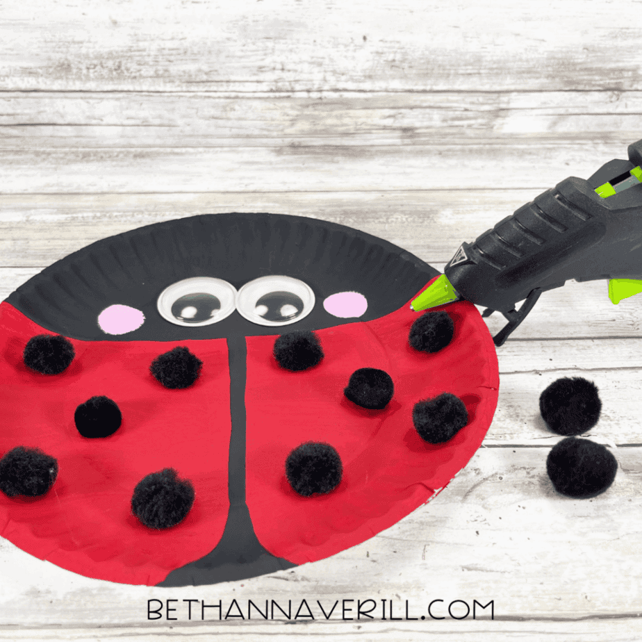 Black pom-poms glued onto the red area to form ladybug spots.