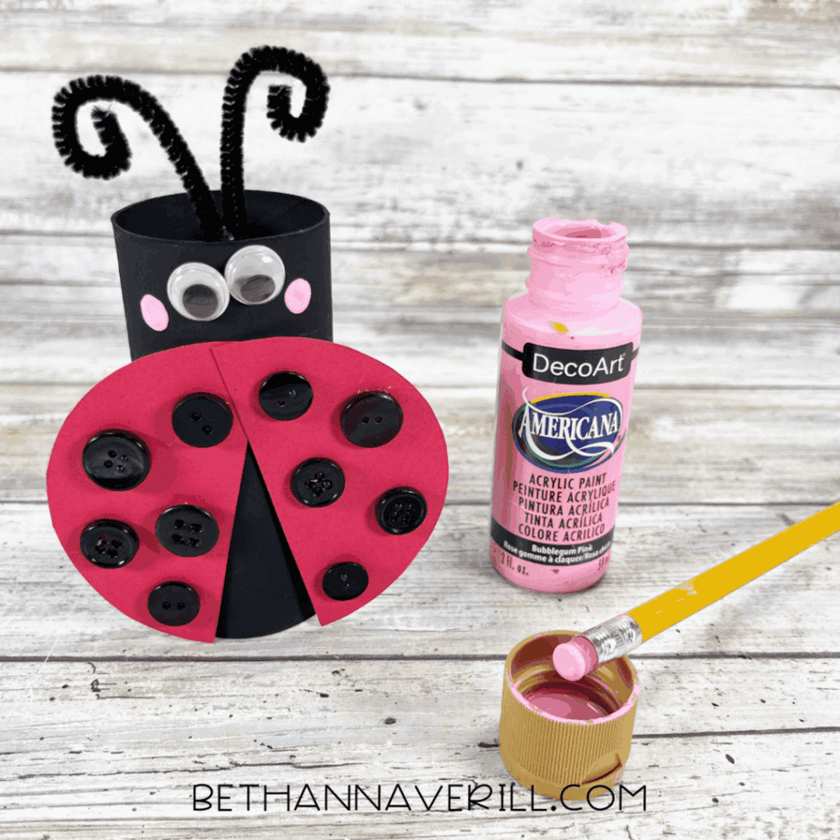 Pink cheeks being painted on the ladybug with a pencil eraser.