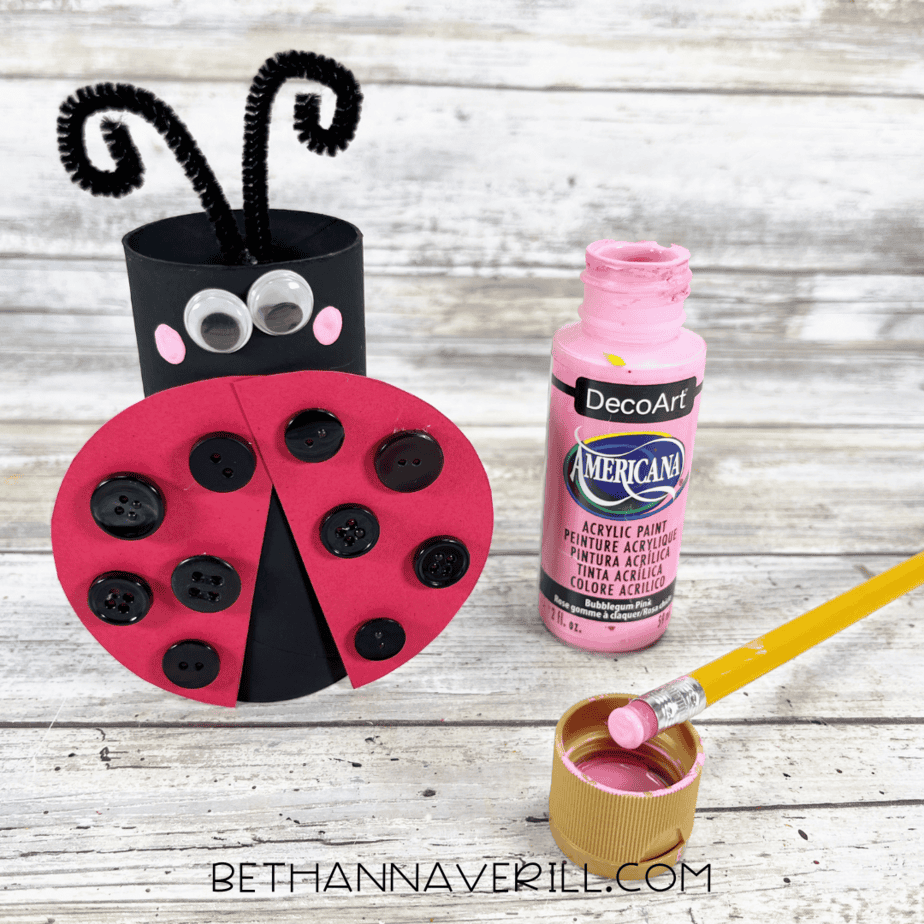 Pink cheeks being painted on the ladybug with a pencil eraser.