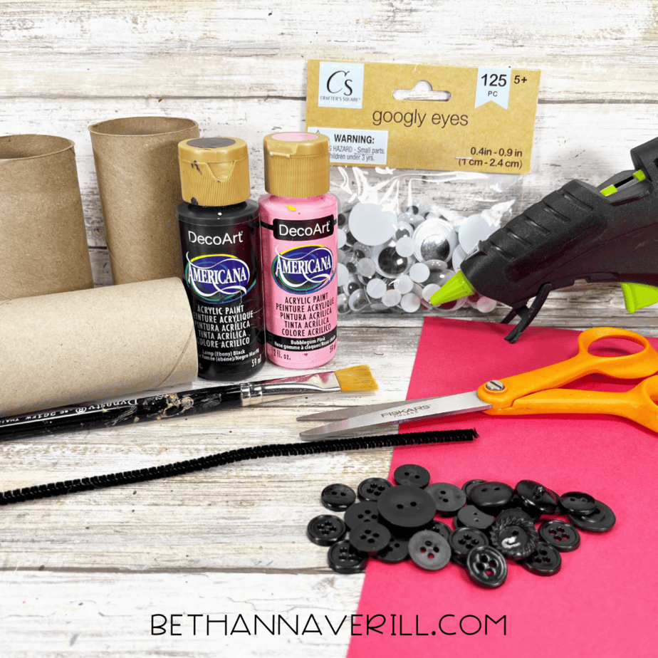 Craft materials for ladybug paper roll craft including toilet paper rolls, paint, buttons, googly eyes, and pipe cleaners.