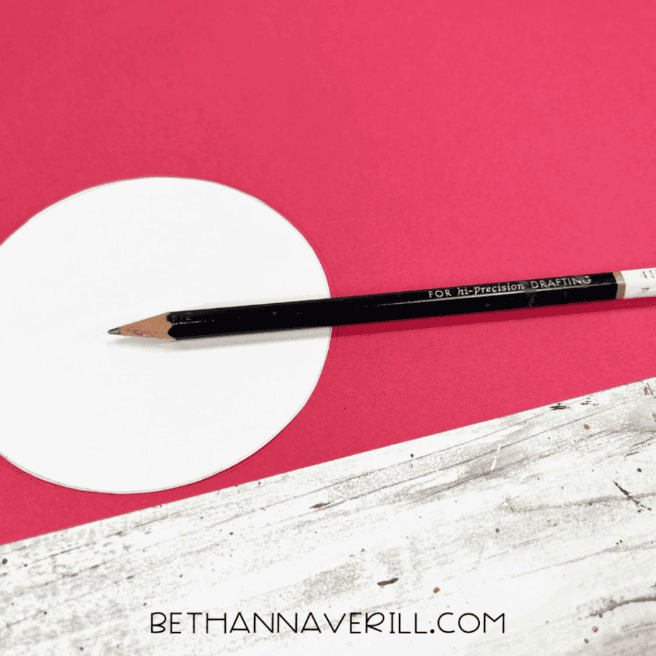 Circle being traced onto red construction paper with a pencil.