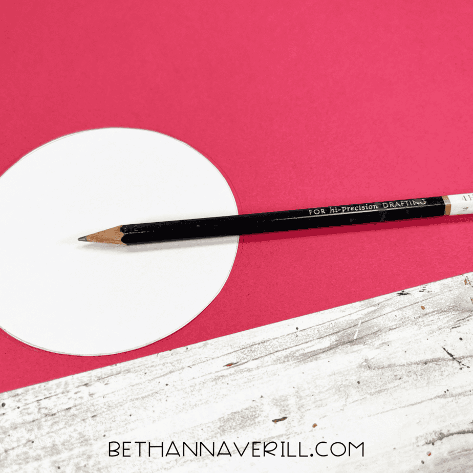 Circle being traced onto red construction paper with a pencil.
