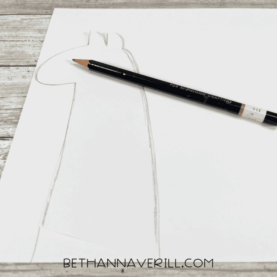 A llama head shape sketched on white cardstock with a pencil.