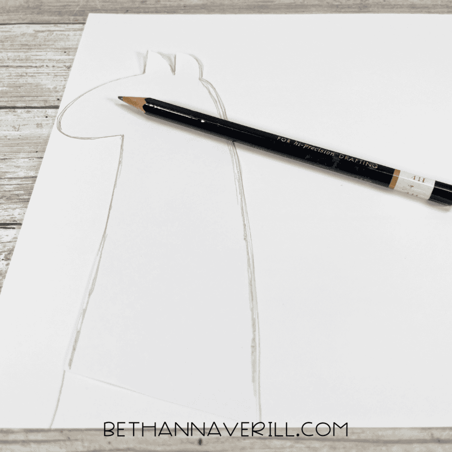 A llama head shape sketched on white cardstock with a pencil.