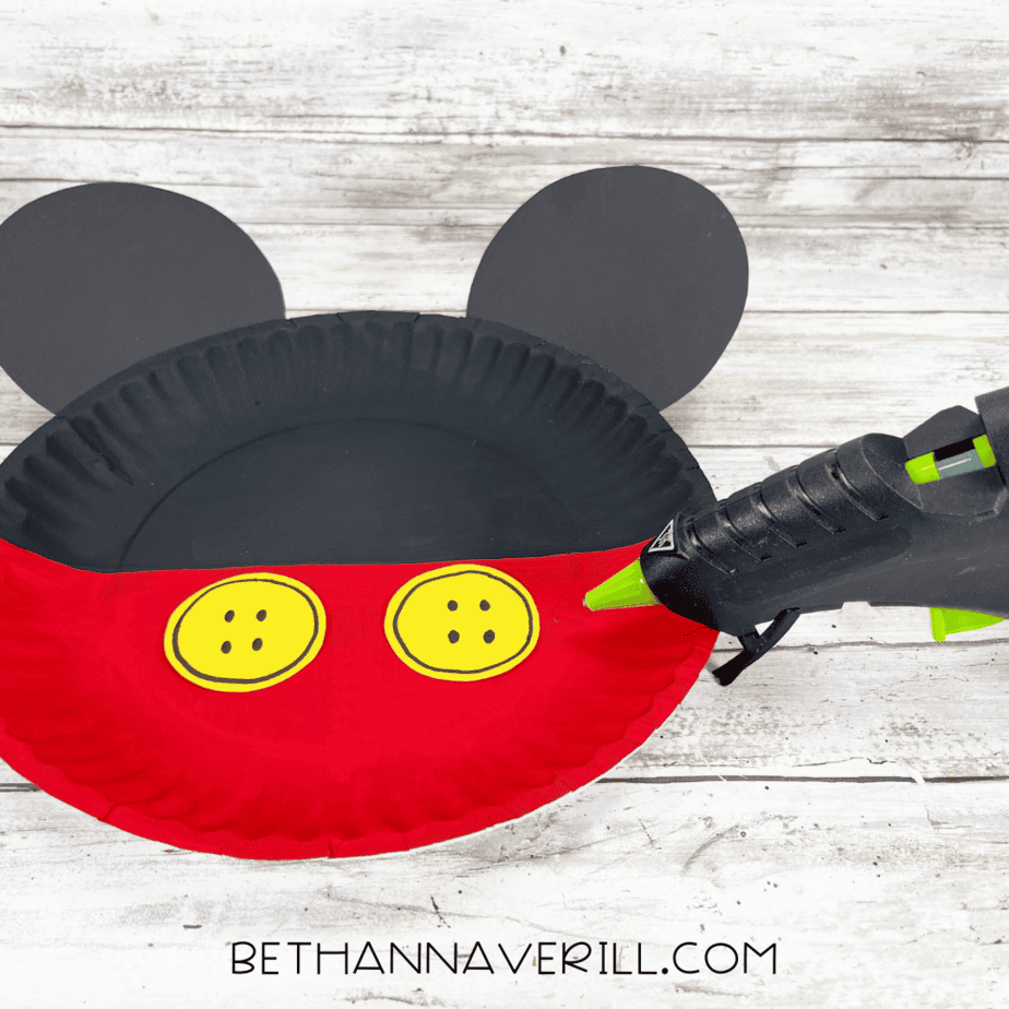 Mickey Mouse paper plate craft with ears and yellow buttons being glued.