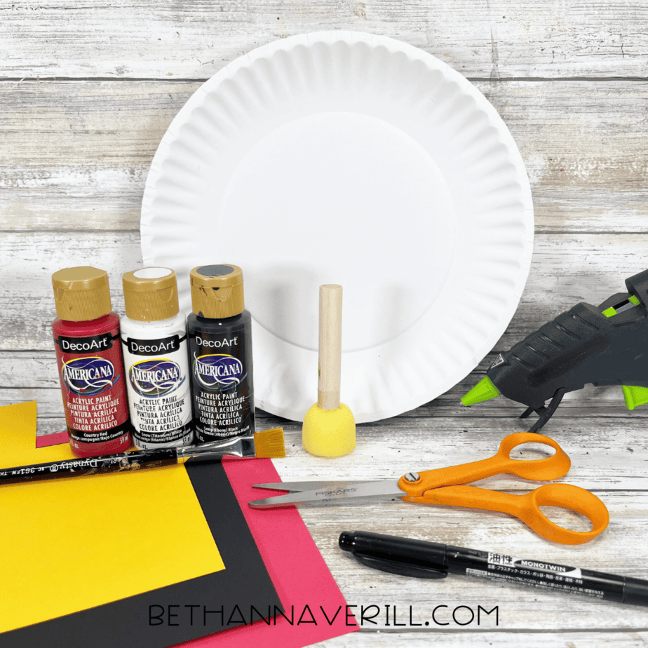 Craft supplies for Mickey Mouse paper plate craft including paints, paper, scissors, glue, and plate.