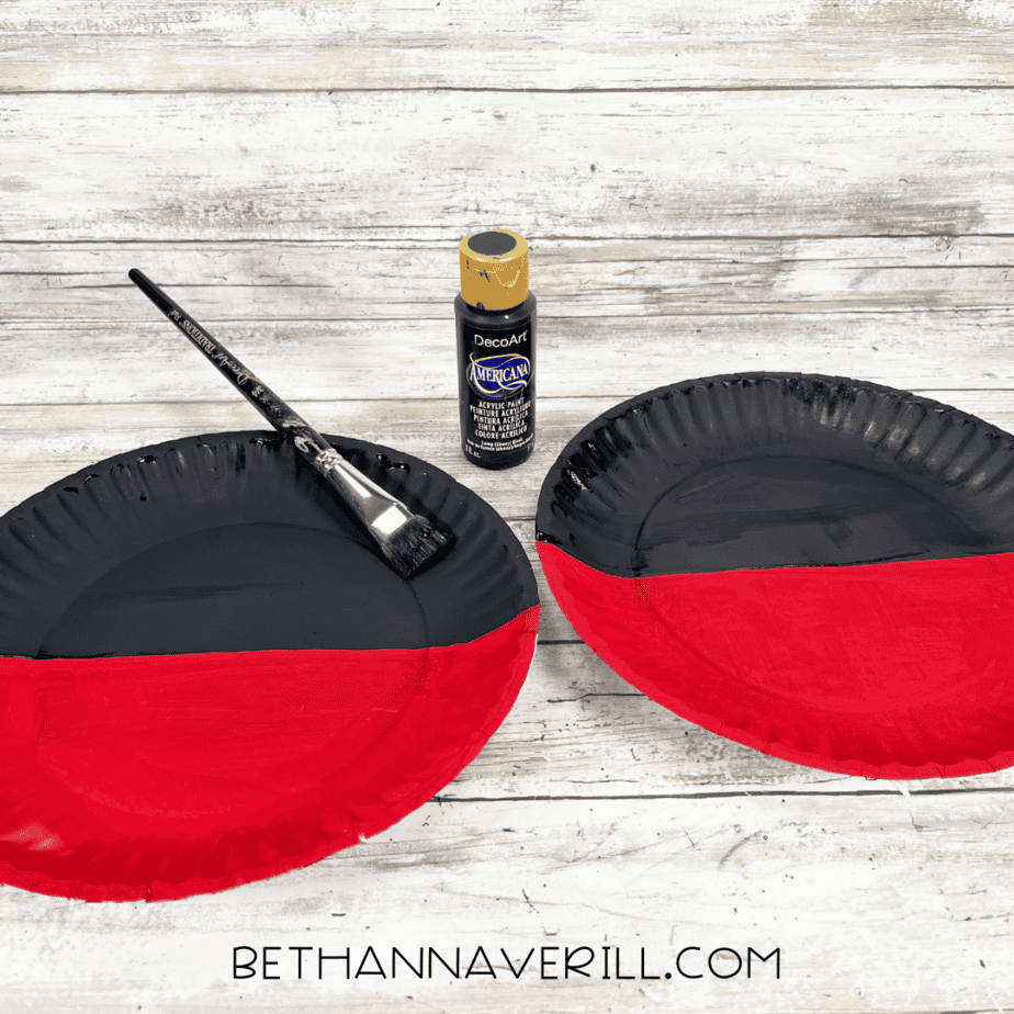 Paper plate with top half painted black and bottom half red.