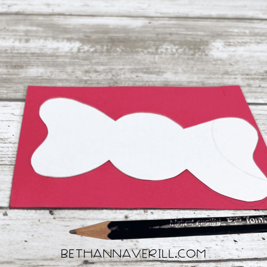 Red construction paper with a bow shape traced in pencil.