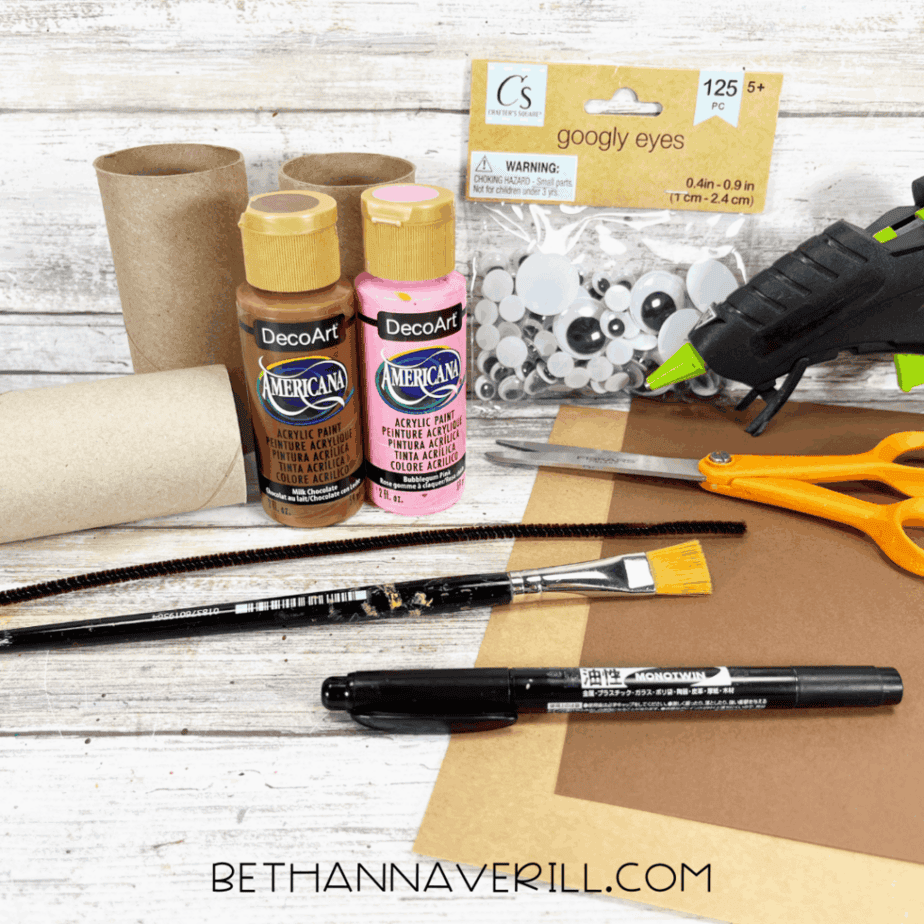 Craft supplies for a monkey paper roll craft, including toilet paper rolls, paints, construction paper, googly eyes, glue gun, scissors, pipe cleaner, and markers.