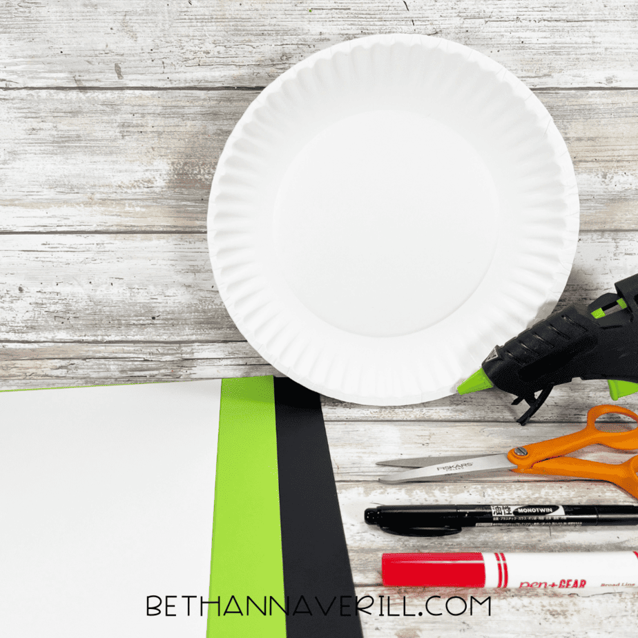 Materials laid out for monster eyes paper plate craft including paper plate, construction paper, scissors, glue, and markers.