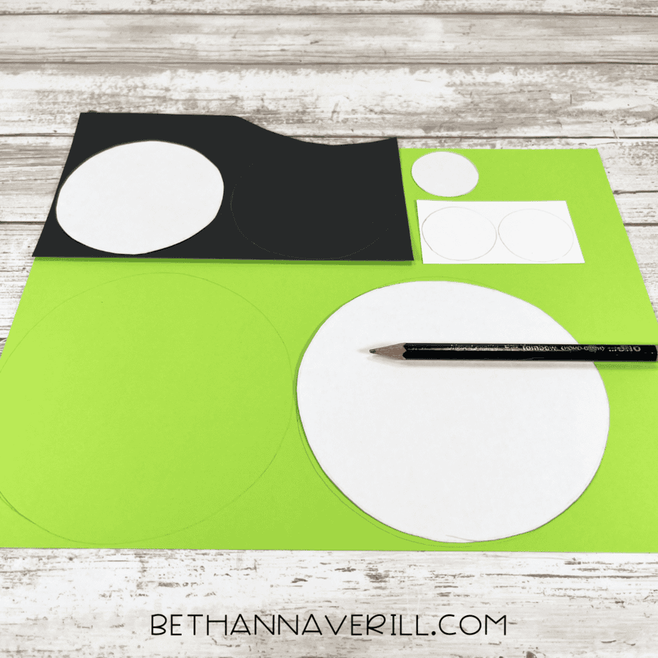 Circles being traced on green, black, and white construction paper with a pencil for the monster eyes craft.