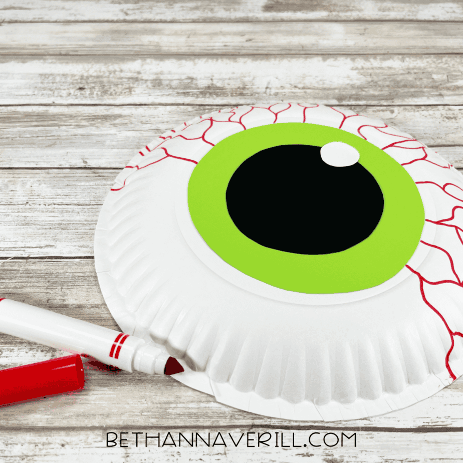 Red marker drawing squiggly bloodshot veins around the monster eye on the paper plate.