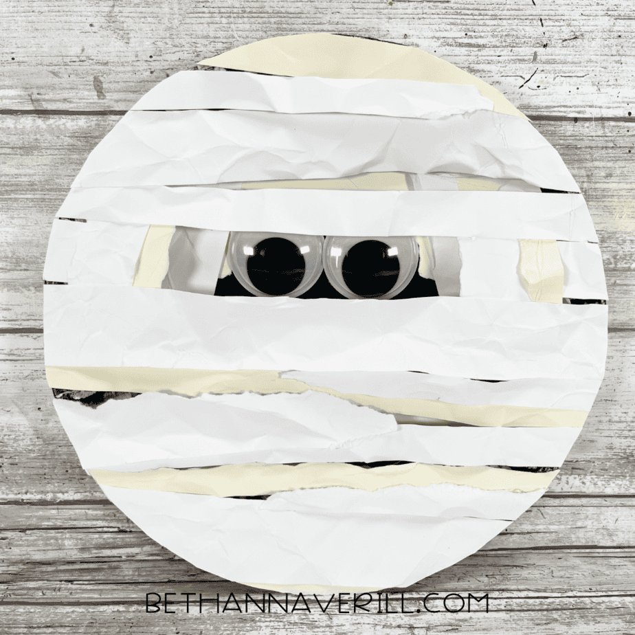 Finished mummy craft with googly eyes peeking through layered white bandages.