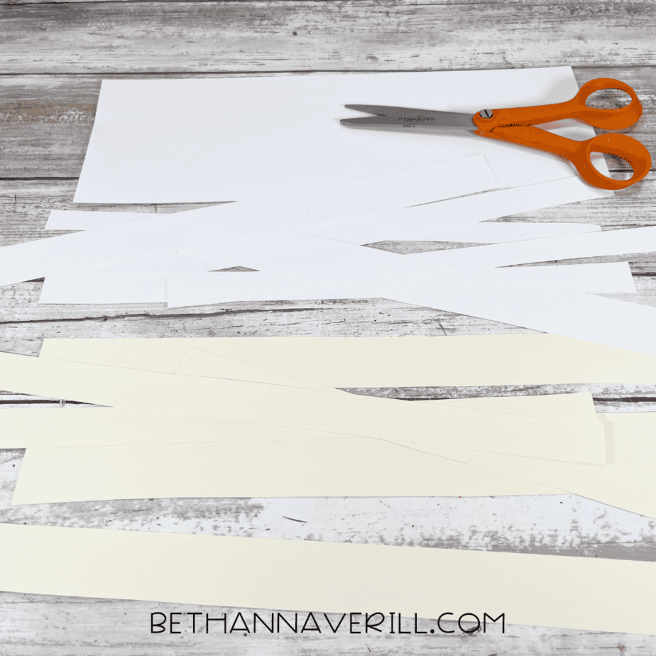 White and cream construction paper cut into strips with scissors beside them.