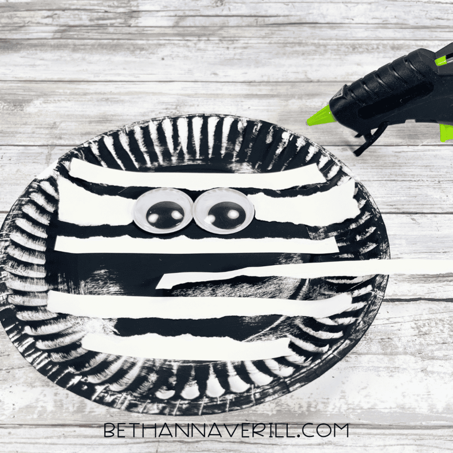 Black paper plate with two googly eyes glued in the center.