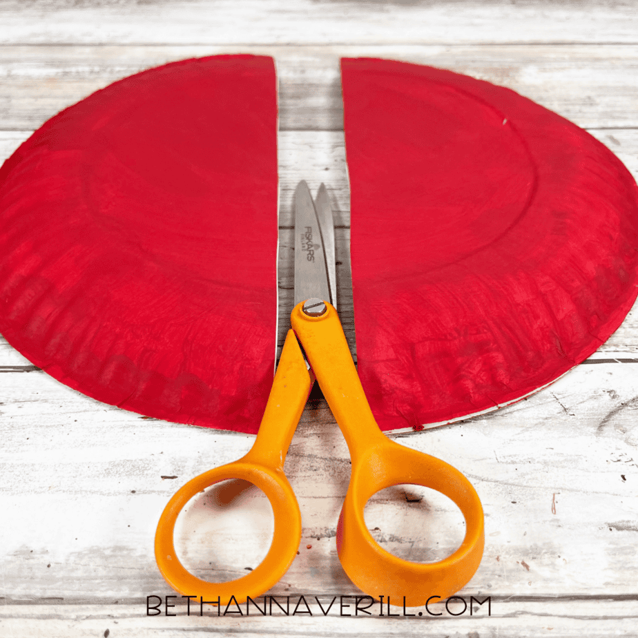 Painted paper plate cut in half with scissors in the center.