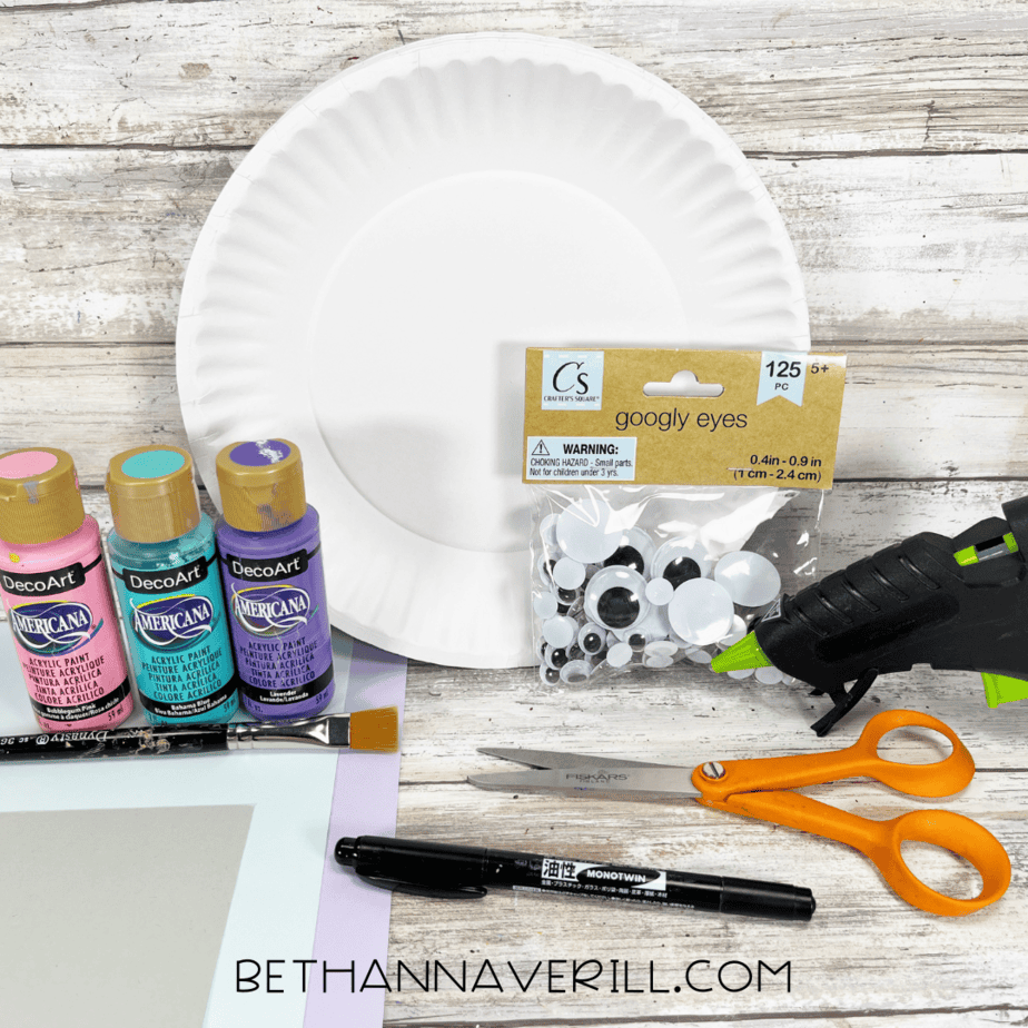 Supplies for narwhal paper plate craft with paint, googly eyes, and paper.
