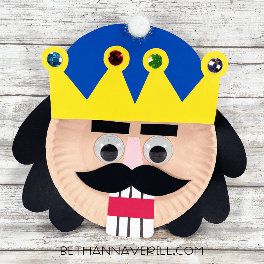 Finished nutcracker paper plate craft with decorated crown, big googly eyes, and mustache.