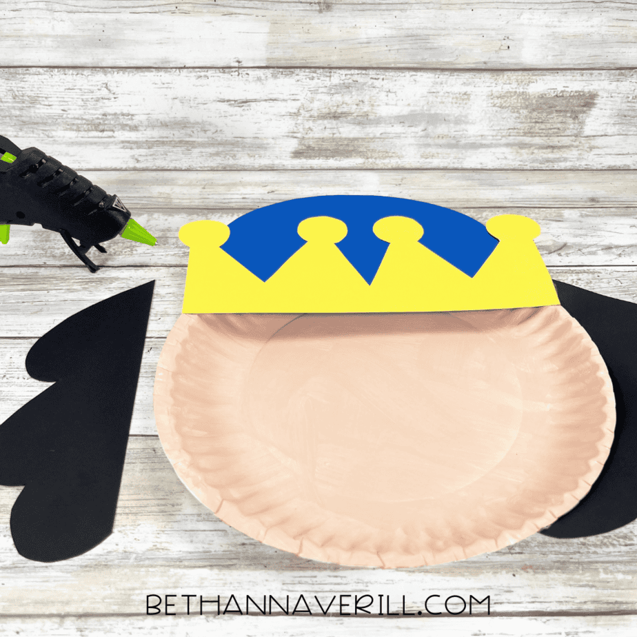 Paper plate with glued yellow and blue crown and black hair pieces on each side.
