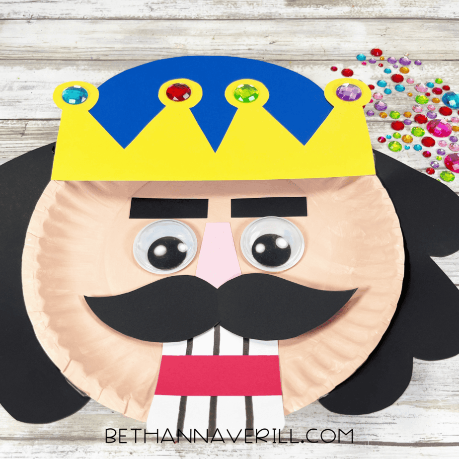 Nutcracker paper plate craft with crown decorated using colorful craft gems.
