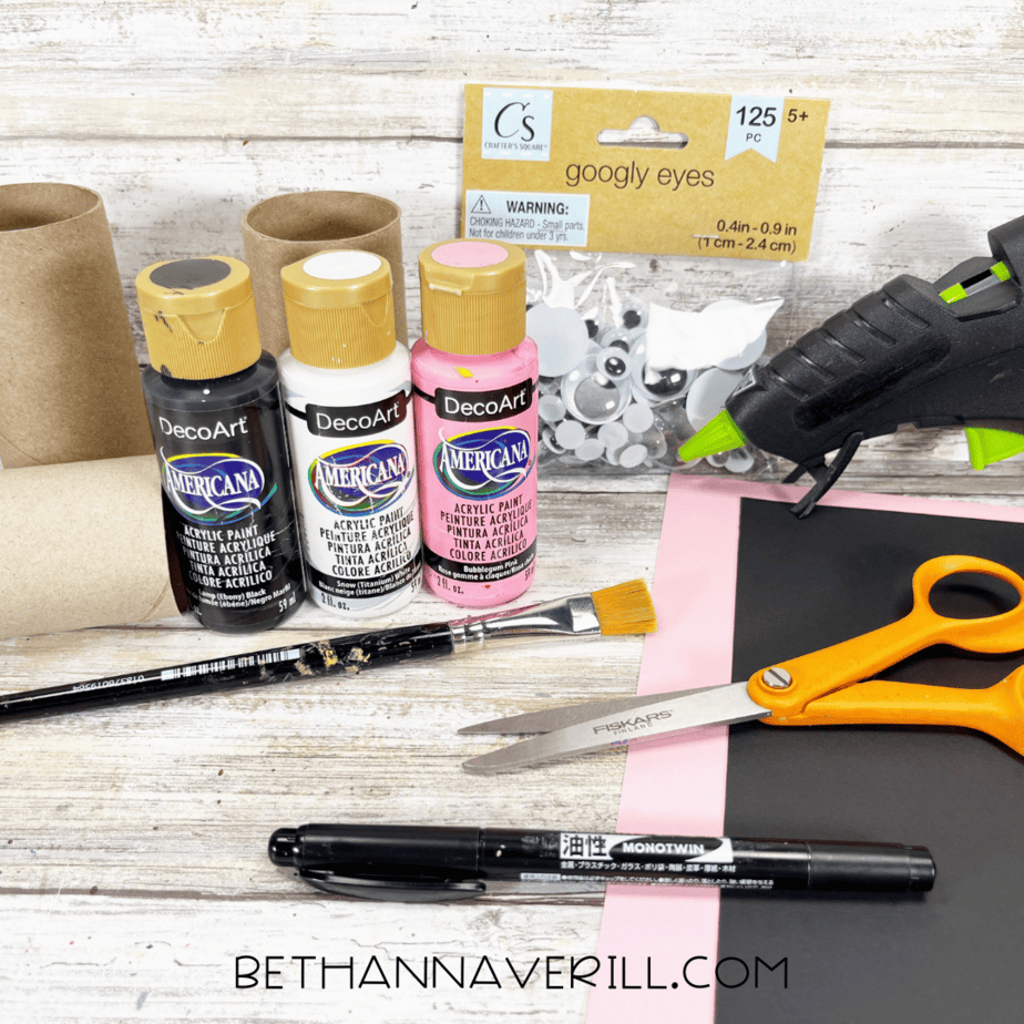 Materials for panda paper roll craft including paint, toilet paper rolls, googly eyes, paper, and glue gun.